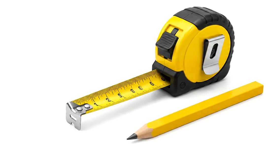 Yellow tape measure pulled out next to a yellow carpenter pencil on a white background