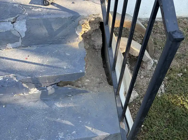 Cracked concrete porch step with a loose rail post, before the repair